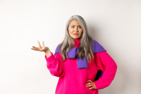 angry-confused-asian-senior-woman-spread-hand-sideways-staring-camera-puzzled-standing-pink-sweater-against-white-background
