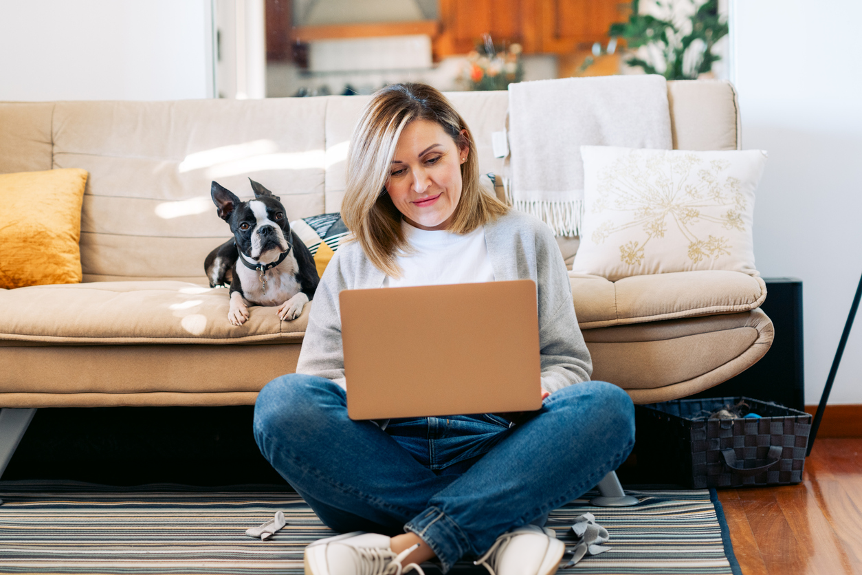 woman sitting on floor with laptop and dog on couch behind her