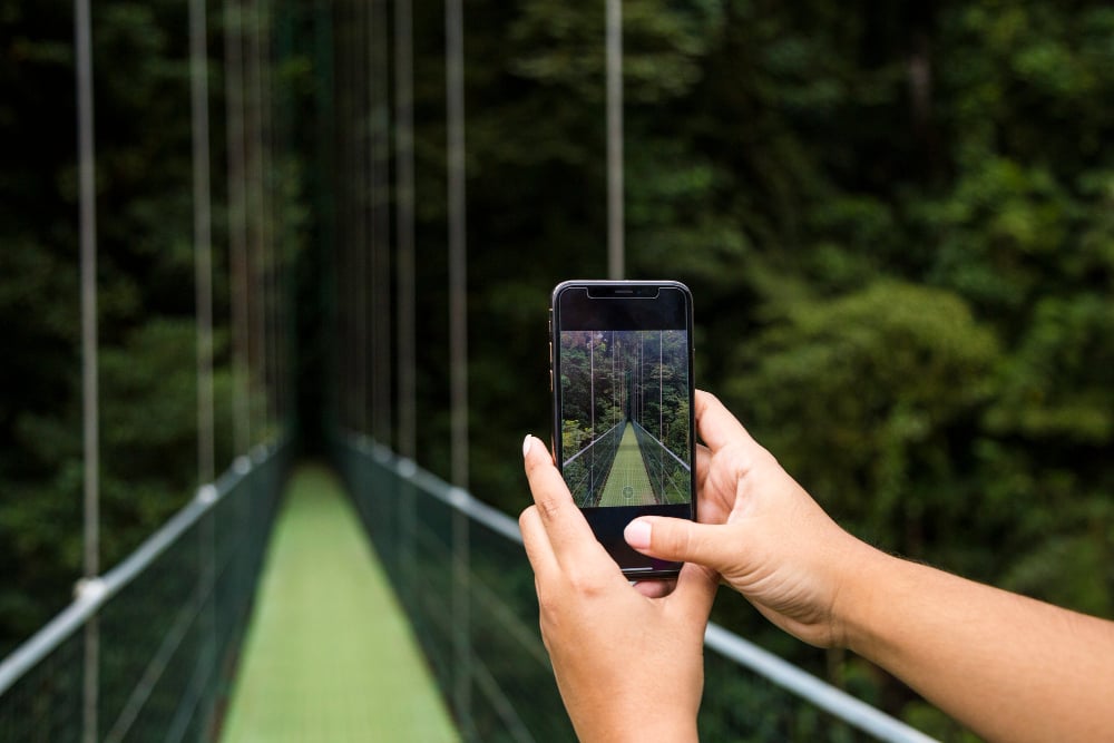 human-hand-taking-picture-suspension-bridge-cellphone-rainforest-costa-rica (1)